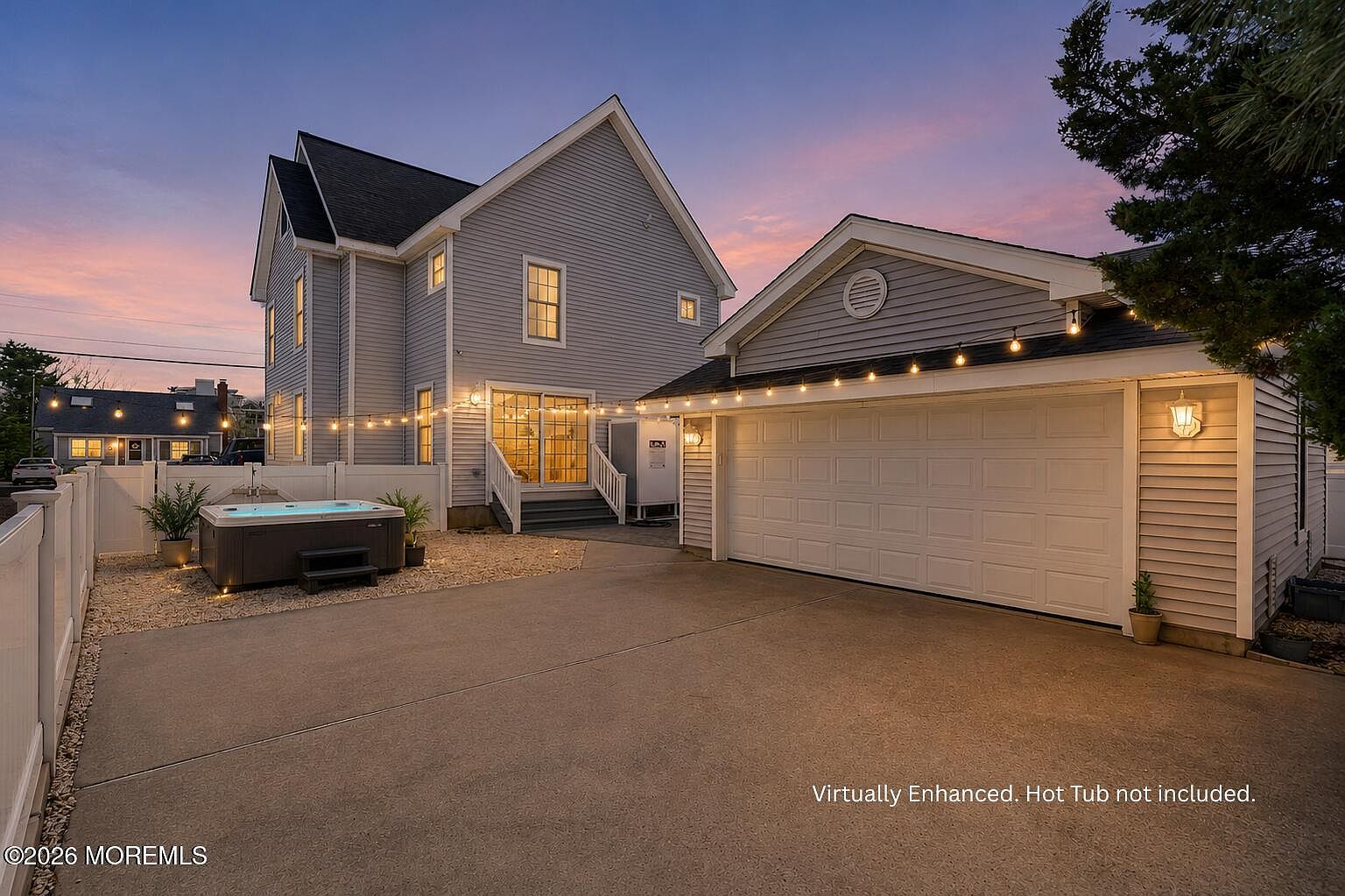 Twilight rear yard of 233 N 7th Street with a hot tub on the patio, café string lights strung across the backyard, the white garage on the right, and a pink dusk sky above