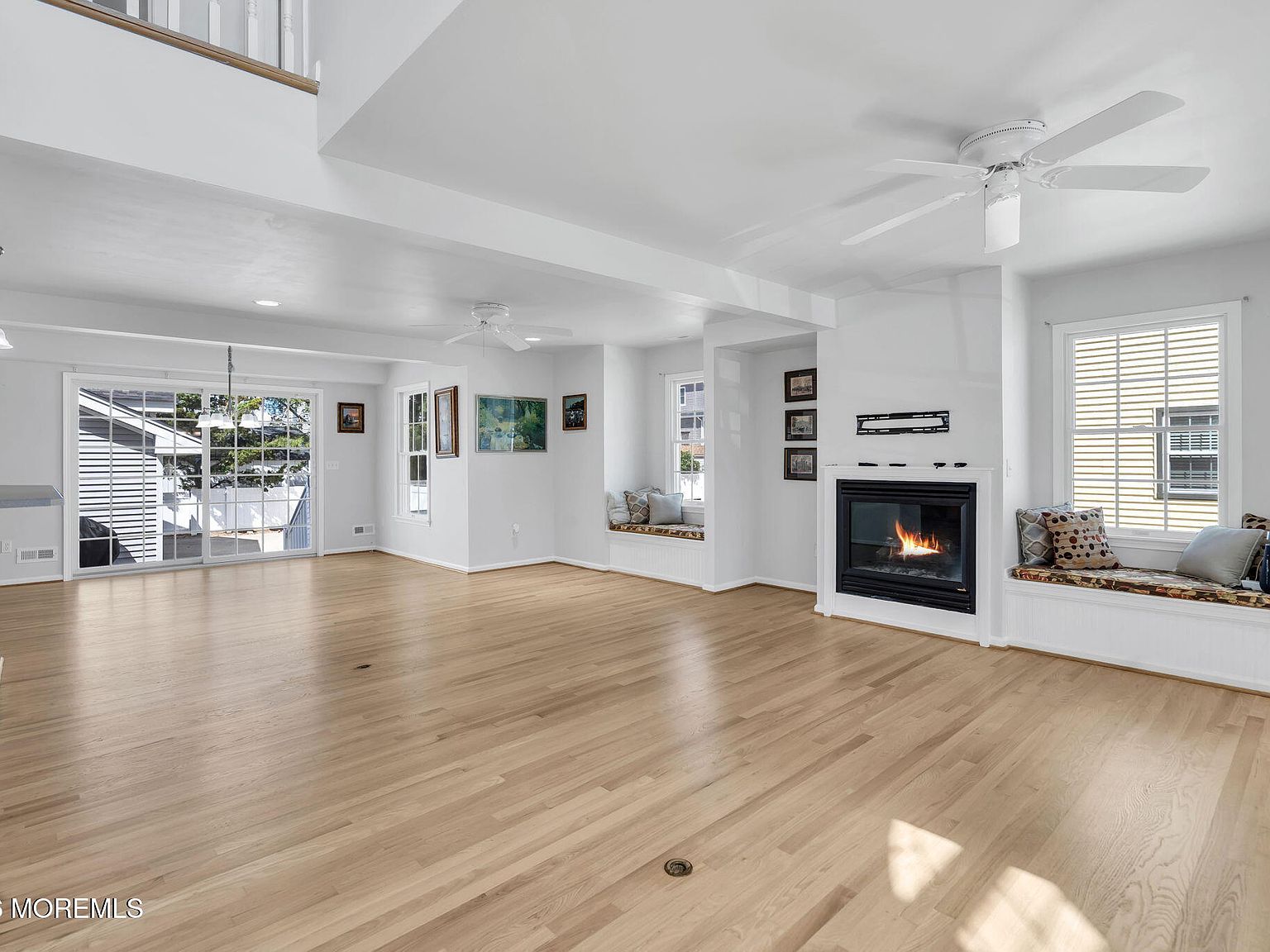 Unfurnished view of the same great room at 233 N 7th Street showing the wood floors, vaulted ceiling, sliding glass doors to the backyard, the fireplace centered between two window seats, and the half-open staircase to the second floor