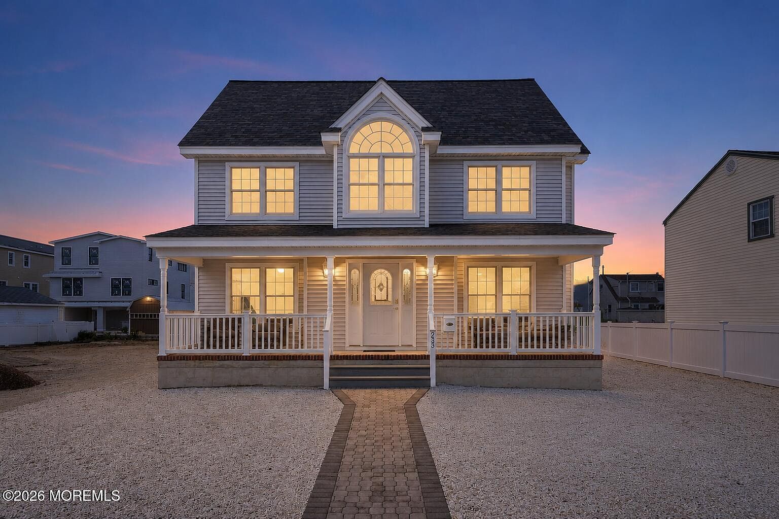 Twilight exterior of 233 N 7th Street, a two-story Surf City colonial with a covered front porch, arched Palladian window, and a pink sunset sky behind the rooftop